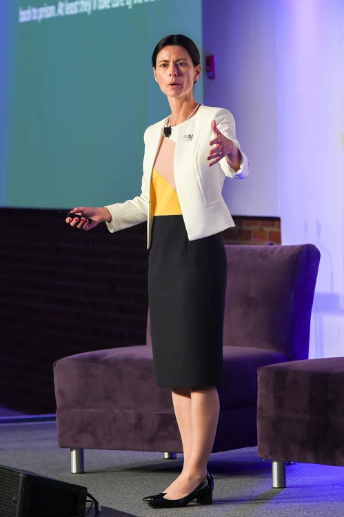 Amy Boutwell, MD, MPP on stage delivering the MAX keynote, gesturing in a white jacket and black dress